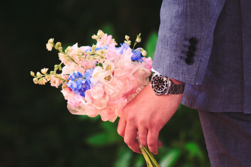groom wearing a watch and holding brides flowers in left hand